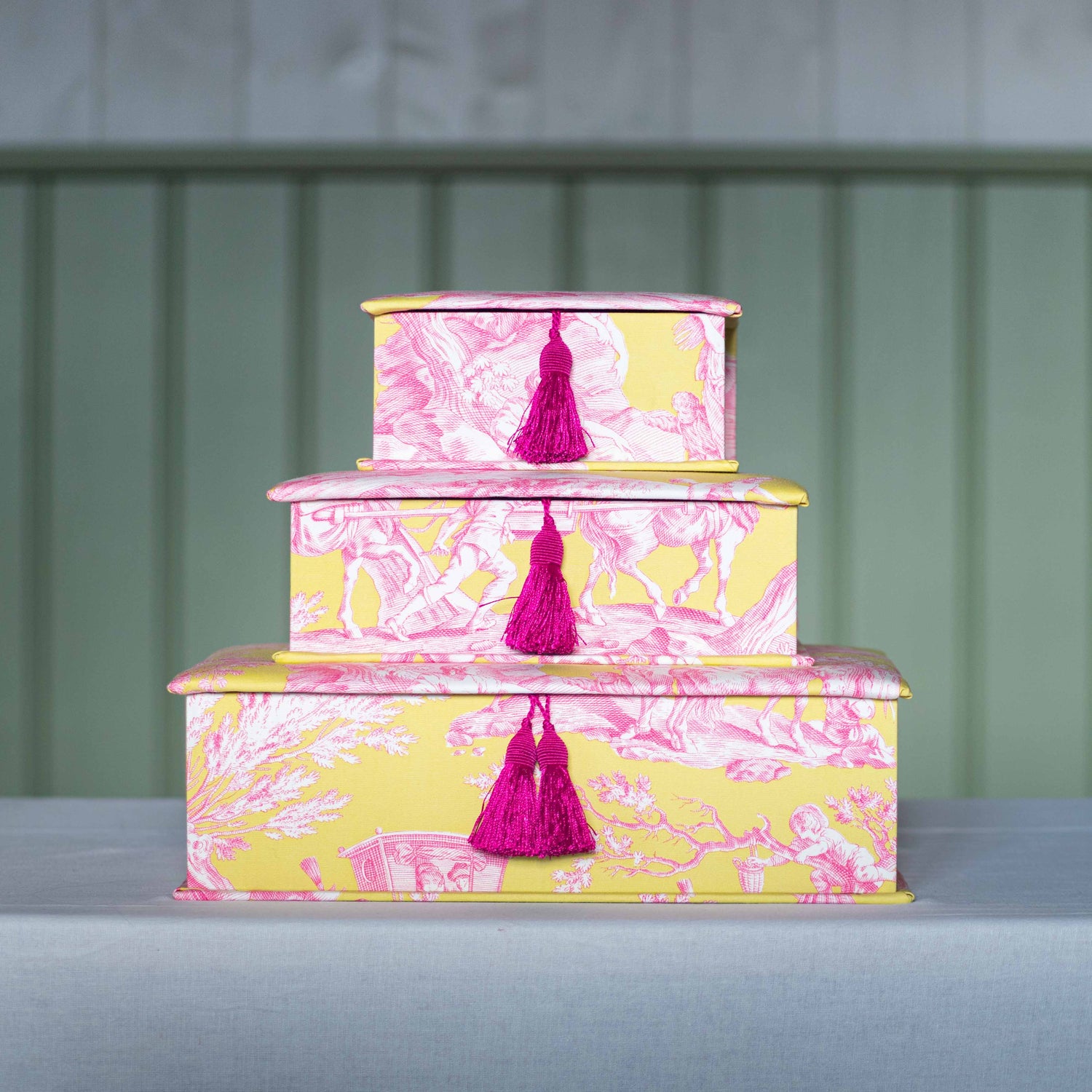 Pyramide von drei handgemachten Schachteln von papierundstoffe aus der Papierwerkstatt in gelb pinkem Toile de Jouy Stoff mit pinker Quaste in den Größen A4, A5 und A6 übereinander