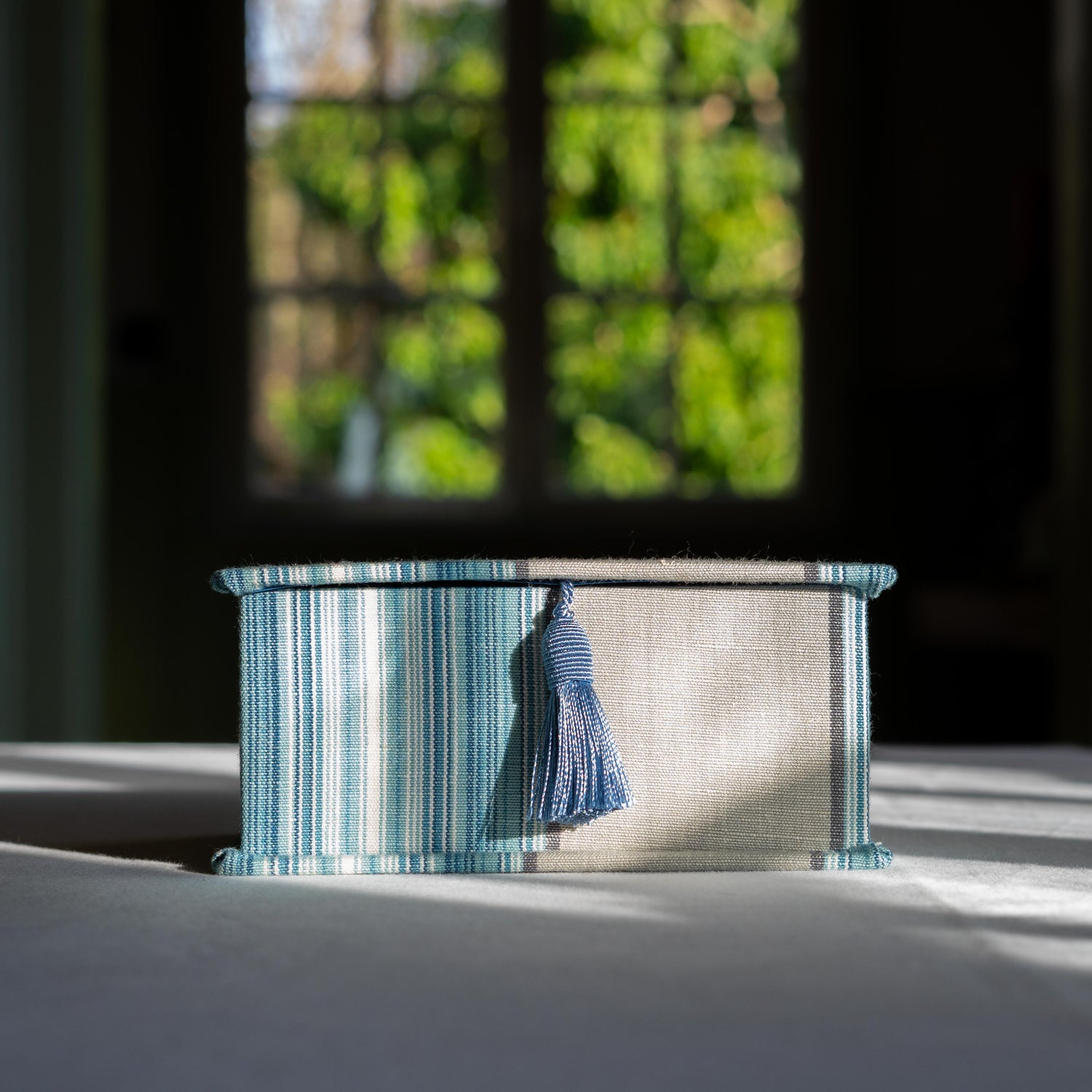 Handgemachte Stoffschachtel von papierundstoffe aus gestreiftem blauem Leinenstoff in der Größe A6 mit blauer Quaste zum Aufbewahren für Erinnerungen.